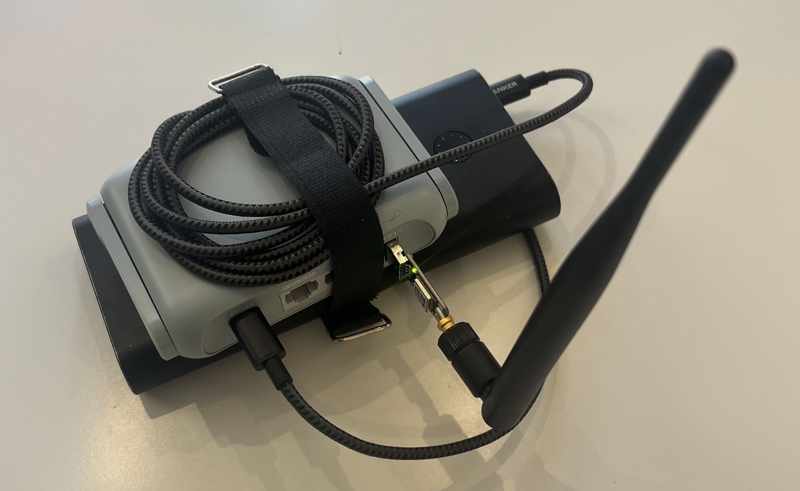 A WiFi router with an additional USB dongle with an antenna attached to it velcroed to a USB powerbank.
